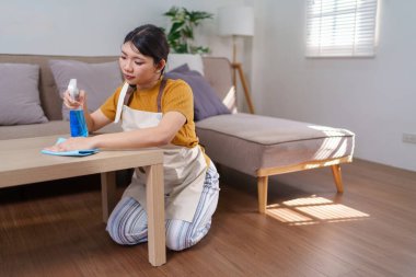 Asyalı bir hizmetçinin, ahşap bir masayı sprey şişe ve mikrofiber bezle temizlerken yakın plan fotoğrafı.