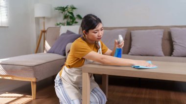 Asyalı bir hizmetçinin, ahşap bir masayı sprey şişe ve mikrofiber bezle temizlerken yakın plan fotoğrafı.