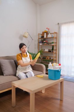 Asyalı hizmetçi rahat bir oturma odasında temizlik yaparken lastik eldiven takıyor.