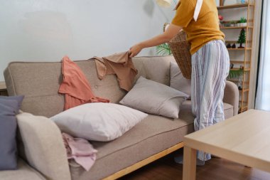 Asyalı hizmetçi rahat bir oturma odasında çamaşır sepetine kıyafet topluyor.