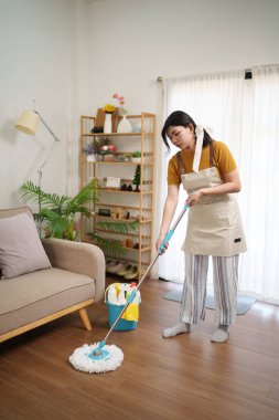 Asyalı hizmetçi modern bir oturma odasında tahta paspas ile yerleri paspaslıyor.