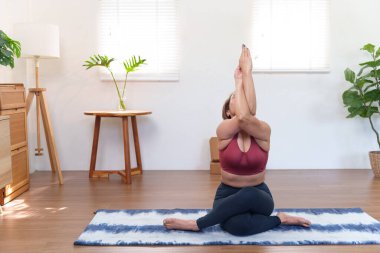 Kıdemli Asyalı kadın Urdhva Hastasana 'ya çalışıyor Yoga minderinde selam duruşu yapıyor rahat bir ev ortamında