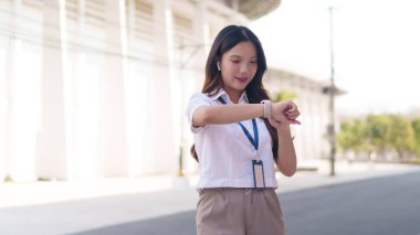 Asyalı iş kadını, modern bir iş alanında dışarıda dururken akıllı saatini kontrol ediyor.