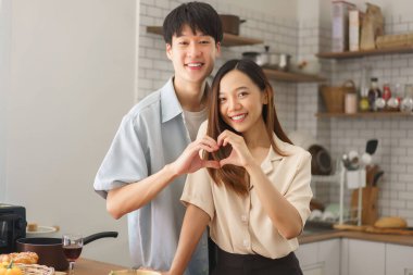 Genç çift mutfakta el hareketleriyle taze yiyecek ve doğal ışıkla çevrili.