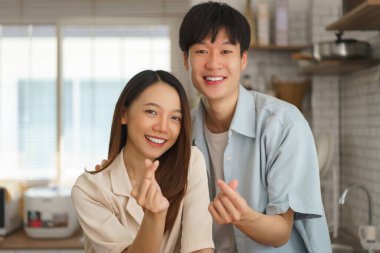 Mutlu çift sıcak mutfakta birlikte yemek yaparken Koreli parmak kalp sembolü gösteriyor.