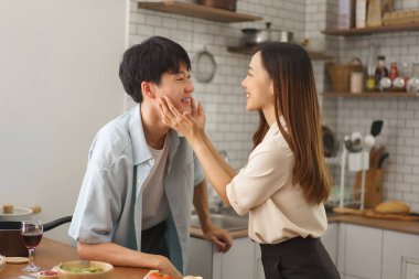 Neşeli çift, sıcak mutfakta taze malzemelerle yemek pişirirken birlikte eğleniyor.