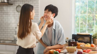 Neşeli çift, sıcak mutfakta taze malzemelerle yemek pişirirken birlikte eğleniyor.