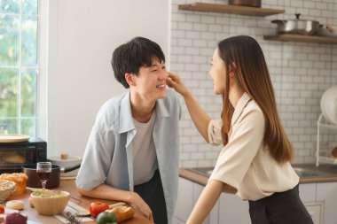Neşeli çift, sıcak mutfakta taze malzemelerle yemek pişirirken birlikte eğleniyor.