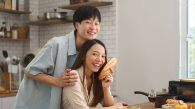 Gülümseyen genç çift, taze yemek ve aşkla dolu modern mutfağa neşeyle poz veriyor.