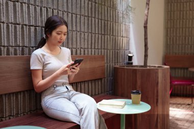 Kadın rahat kafeterya masasında akıllı telefonlara bakarken huzur içinde kahve molası veriyor.