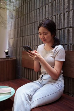 Kadın rahat kafeterya masasında akıllı telefonlara bakarken huzur içinde kahve molası veriyor.