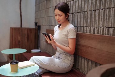 Kadın rahat kafeterya masasında akıllı telefonlara bakarken huzur içinde kahve molası veriyor.