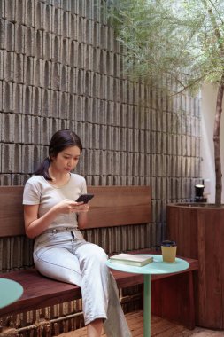 Kadın rahat kafeterya masasında akıllı telefonlara bakarken huzur içinde kahve molası veriyor.