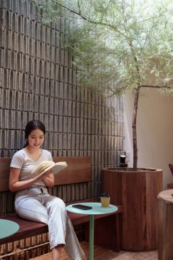 Huzurlu genç kadın günlüğünü okuyor ve sakin bir anda açık hava kafesinde yansıtıyor.