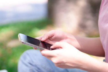 Açık havada akıllı telefonunu kullanan Asyalı genç bir kadının yakın çekimi. Mobil öğrenme, çevrimiçi eğitim, bilgi erişimi ve dijital eğlence, günlük tarz ve iletişim üzerine odaklanın.