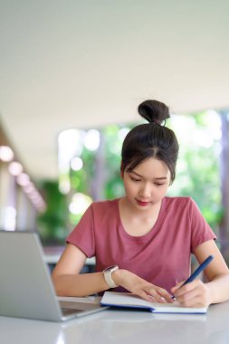 Genç Asyalı bir kadın evde dizüstü bilgisayar kullanıyor ve not defteri yazıyor. Öğrenci öğrenimi için uzaktan eğitim kavramı, üniversite ya da üniversite. Eğitim ve teknolojiye odaklan.