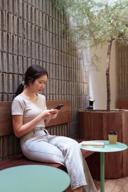 Kadın rahat kafeterya masasında akıllı telefonlara bakarken huzur içinde kahve molası veriyor.