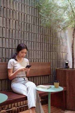 Kadın rahat kafeterya masasında akıllı telefonlara bakarken huzur içinde kahve molası veriyor.