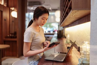 Gündelik mali planlama oturumunda laptopta çalışan ve kafe kasasında hesap makinesi kullanan bir kadın.