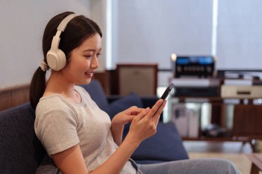 Kanepede oturup kulaklıkla müzik dinleyen ve akıllı telefondan şarkı okuyan genç bir kadın.