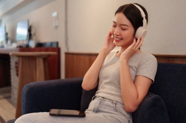 Kanepede oturup kulaklıkla müzik dinleyen ve akıllı telefondan şarkı okuyan genç bir kadın.