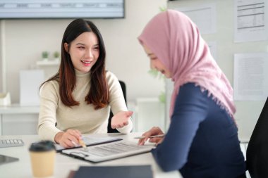Biri tesettürlü iki genç iş kadını mali belgeler üzerinde işbirliği yapıyor. Yatırım stratejilerini tartışıyor ve İslami finans ile ilgili içerik için uygun bir ofis işyerindeki verileri analiz ediyorlar.
