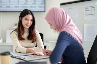 Biri tesettürlü iki genç Asyalı kadın, bir ofiste bir Müslüman iş projesinde işbirliği yaparak, başarı için strateji ve takım çalışmasını tartışıyor. İş Kadını Toplantısı.