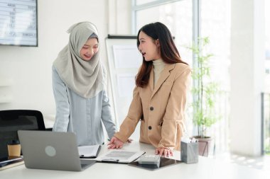 Modern bir ofiste iş belgeleri üzerinde çalışan iki genç Asyalı kadın. Stratejileri tartışmak, raporları incelemek, takım çalışması, finansal veri sunumu. Profesyonellik ve başarı.