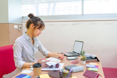 Asyalı bir iç mimar masasında çalışıyor. O, bir sonraki tasarım projesini planlarken renk örnekleri, bir defter ve bir dizüstü bilgisayarla çevrilidir. Çalışma alanı, iç tasarım kavramı.