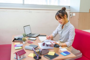 Genç Asyalı kadın iç mimar masasındaki renk örneklerini inceliyor. Hayalinizdeki ev için ilham verici modern ev tasarımları, uzay planlaması ve profesyonel tasarımcı danışmanlığı.