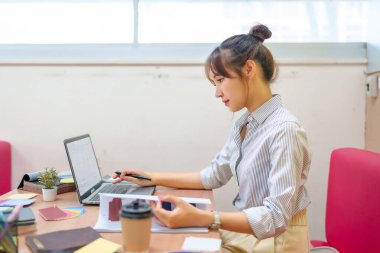 Asyalı genç kadın bilgisayarını kullanarak internetten çalışıyor. Kitaplar, kahve ve eğitim malzemeleriyle dolu bir masada oturuyor. Bu resim e-öğrenim, öğrenci ve çevrimiçi eğitim içeriği için idealdir..