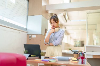 Görüntü, modern ofis ortamında dizüstü bilgisayarına özenle bakan genç bir Asyalı kadını, çevrimiçi öğrenme, eğitim ortamları veya yaratıcı çalışma alanlarını göstermek için ideal hale getiriyor..