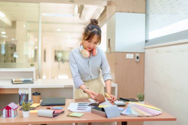 Asyalı genç iç mimar kadın ofis masasında kumaş örnekleri ve renk paletleri ile çalışıyor. Ev yenileme projeleri, güzel ve işlevsel alanlar için malzeme seçiyor..