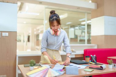 Asyalı kadın iç mimar, renk örnekleri ve malzeme örnekleriyle fikirler çiziyor. Modern ofis çalışma alanı, yaratıcı genç bir profesyonel, ev dekorasyonu ve yenileme için tasarım süreci.