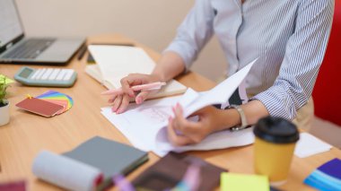 Genç Asyalı kadın iç mimar masasında çalışıyor. Planları, renk örneklerini ve tasarım fikirlerini inceliyor. Bu resim bir profesyoneli iş başında yakalar, iç tasarım planlarını geliştirir.