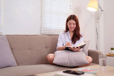 20 'li yaşlarda genç bir kadın evdeki bir kanepede dinlenirken günlük yazmaktan zevk alıyor. Günlük tutmak, çalışmak ya da yaratıcı işler için sakin, odaklı bir ortam.