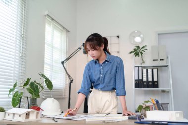 Asyalı kadın mimar parlak ofisin planlarını tasarlıyor. Genç yetişkin mimar inşaat projesi için planlar tasarlıyor. İnşaat planları üzerinde çalışan kadın mühendis..