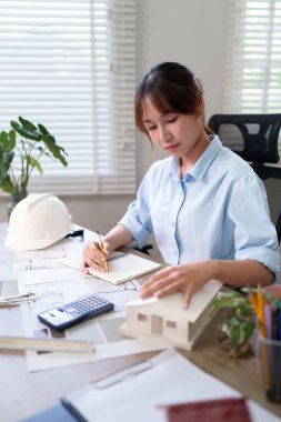 Genç bir Asyalı mimar ofisinde tasarımlar üzerinde çalışıyor, bir bina modelini dikkatlice inceliyor ve planlar çiziyor. Bu onun en iyi mimar olarak yeteneklerini ve mimarlık kariyerine olan bağlılığını vurguluyor. En iyi mimar kariyerini keşfedin.