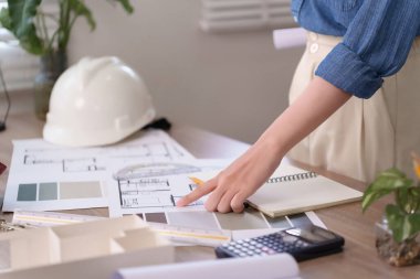 Asyalı kadın mimarın elleri titizlikle masanın üzerindeki planı işaret ediyor. Yeni ev projesi için inşaat planını gözden geçiriyorum. Planlama için ev projesinin planını detaylandır. Bu resim Asyalı kadınların ev yapımında kullandıkları detayları ve işlemleri kaydeder.
