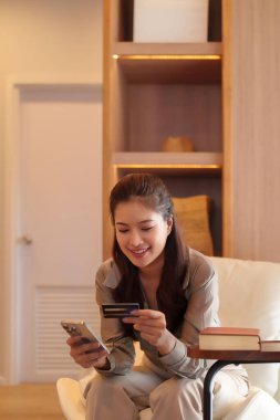 Genç Asyalı kadın online alışveriş için akıllı telefon ve kredi kartı kullanıyor. Mutlu kadın, güvenli işlemler için cihazına ödeme yapıyor. Modern bankacılık..