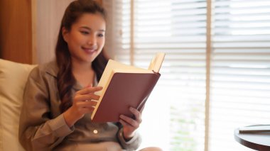 Kişisel gelişim ve bilgi için rahatça kitap okuyan Asyalı bir kadın. Bir kadının barışçıl ifadesi, okuduğu kitaptaki derin deneyimi ima eder.