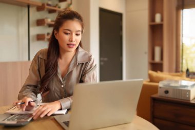 Asyalı bir kadın çalışmak için bilgisayar ve kalemle finansal analiz yapıyor. Bu yetişkin kadın strateji için yatırımları ve borsa verilerini yönetiyor..