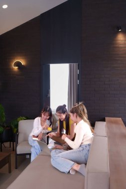 Üç genç Asyalı kadın, modern bir oturma odasında dizüstü bilgisayar ve kredi kartıyla online alışveriş yapmayı seviyor. Satın alma ve planlamayı birlikte tartışan bu arkadaşlar boş zamanı ve dostluğu paylaşıyor ve sıcak bir atmosfer yaratıyorlar..