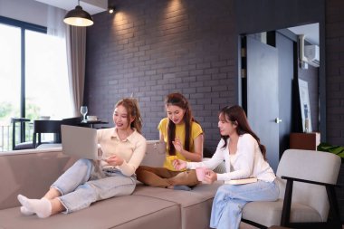 Üç genç Asyalı kadın evde kredi kartı kullanarak internetten alışveriş yapıyor. Bu kavram, arkadaşlık yaşam tarzı teknolojisini, ticareti ve rahatlamayı temsil ediyor.