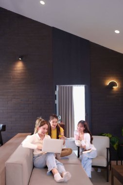 Asyalı bir grup kadın evde dizüstü bilgisayar ve kredi kartı kullanarak kolay alışverişin keyfini çıkarıyorlar. Mutlu arkadaşları olan modern yaşam tarzlarını satın almak veya indirim yapmak için mutlu ve heyecanlı görünüyorlar.