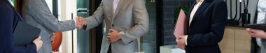 Bir grup iş arkadaşı, Asyalı kadın ve erkek, ofiste anlaşma ve ortaklığı simgeleyen el sıkışıyorlar. Ellerinde dosya ve tablet gibi belgeler var..
