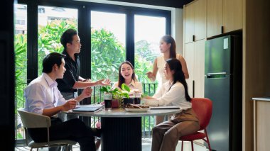 Bu resim, Asyalı iş adamlarının doğal ışık ve yeşillik dolu modern ofis ortamında ortak bir toplantı yaptıklarını gösteriyor..