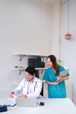 Asyalı doktor ve hemşirelerden oluşan bir ekip, sağlık hizmetleri için ekip çalışmalarını gülümseyerek ifade eden hasta tıbbi kayıtlarını görüşmek için hastane ofisinde birlikte çalışıyorlar.