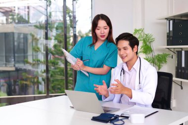 İki yetişkin Asya 'lı doktor ve hemşire, hasta bakımı konusunda işbirliği yapıyorlar. Modern ve parlak bir klinikte dizüstü bilgisayar kullanıyorlar. Ekip çalışması ve sağlık hizmetlerinde mükemmellik sağlıyorlar.