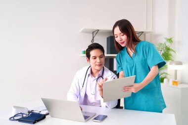 Asyalı yetişkin doktor ve hemşire, parlak bir klinik ortamında dizüstü bilgisayar kullanarak hasta verilerini gözden geçiriyorlar. Sağlık, tıp ve profesyonel takım çalışması projeleri için ideal.